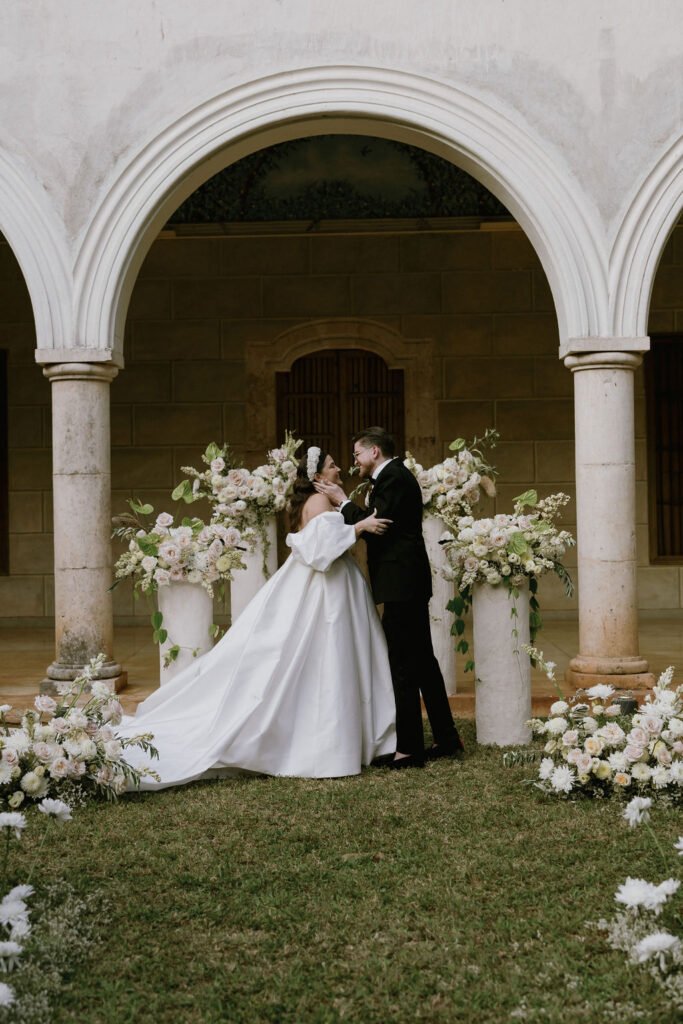 The couple beneath a stone arch flanked with white flowers