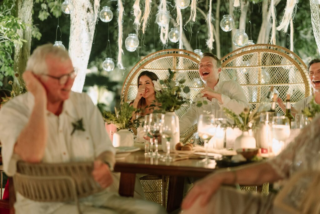 Guests laughing around a candlelit table under hanging lights