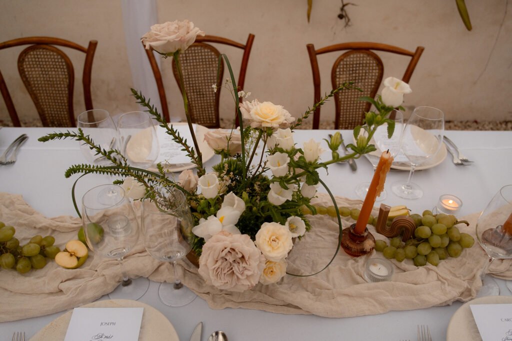 A tablescape of roses, grapes and tapered candles running along a linen runner
