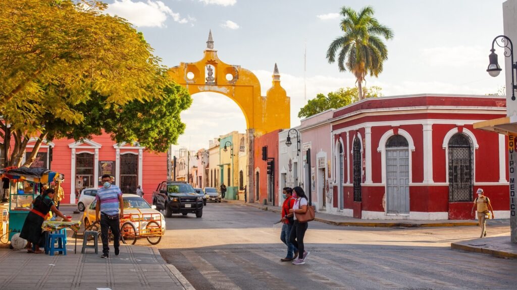 The yellow arch in Mérida, with painted colonial houses and a street vendor beside it